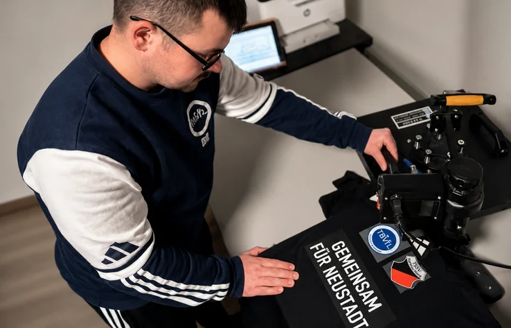 Matze arbeitet an einer Transferpresse und veredelt ein schwarzes Textil